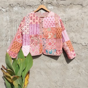 May include: A pink and white patchwork quilted jacket with a button closure. The jacket is made of cotton and has a relaxed fit.