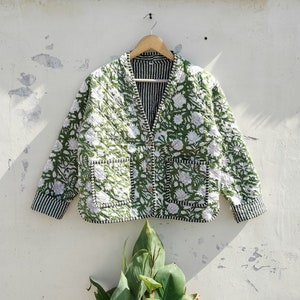 May include: A green quilted jacket with a white floral print and black and white striped sleeves. The jacket has a button closure and two pockets.
