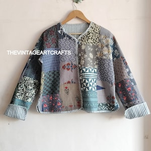 May include: A patchwork quilted jacket in a blue, green and grey colour scheme. The jacket has a button fastening and long sleeves. The text "THEVINTAGEARTCRAFTS" is visible on the front of the jacket.