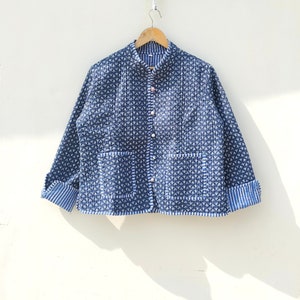 May include: A blue quilted jacket with a white floral pattern and white piping. The jacket has a mandarin collar, a button closure, and two patch pockets.