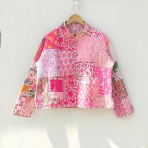 Pode incluir: Uma jaqueta acolchoada de patchwork rosa e branca com gola mandarim e mangas compridas. A jaqueta é feita de um tecido macio e leve e tem um caimento solto.