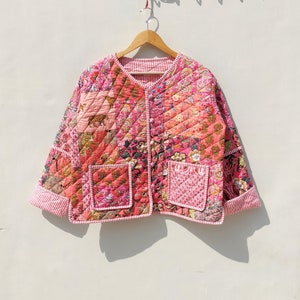 May include: A pink quilted jacket with a floral and animal print. The jacket has a button closure and two pockets.