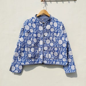 Puede incluir: Una chaqueta acolchada azul con un estampado floral blanco. La chaqueta tiene un cuello mandarín, cierre de botón y mangas largas.