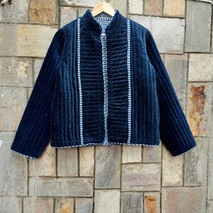 May include: A navy blue quilted jacket with vertical striped accents and a mandarin collar. The jacket has a button-up front and is hanging on a wooden hanger. The jacket's design features a textured, ribbed pattern.