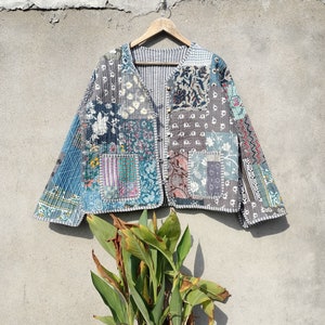 Pode incluir: Uma jaqueta de patchwork com uma variedade de cores e padrões, incluindo azul, cinza e branco. A jaqueta tem um fecho de botão e uma gola.