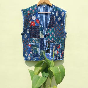 Peut inclure: Un gilet matelassé bleu avec un motif patchwork floral. Le gilet a un col en V et une fermeture à nouer.
