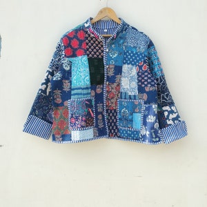 Pode incluir: Uma jaqueta acolchoada azul com um design de patchwork que apresenta vários padrões florais em tons de azul, vermelho e branco. A jaqueta tem um colar mandarim e um fecho de correr.