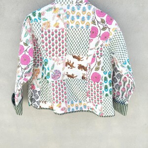 May include: A white quilted jacket with a patchwork design featuring floral and tiger motifs. The jacket has pink flowers, green leaves, and a striped cuff. The overall style is bohemian.