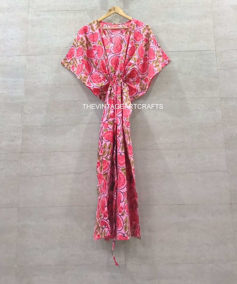 May include: A pink and green floral print kaftan with a deep V-neckline and a tie at the waist. The kaftan has short, wide sleeves and a flowing skirt.