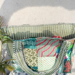 May include: A large green and white striped tote bag made from patchwork fabric. The bag has two handles and is made from a variety of different fabrics, including green, blue, pink, and white.