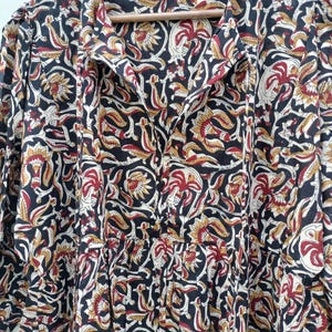 May include: A long-sleeved dress with a floral pattern in black, red, and gold. The dress has a collared neckline and buttons down the front. The fabric appears to be lightweight, suitable for warmer weather.