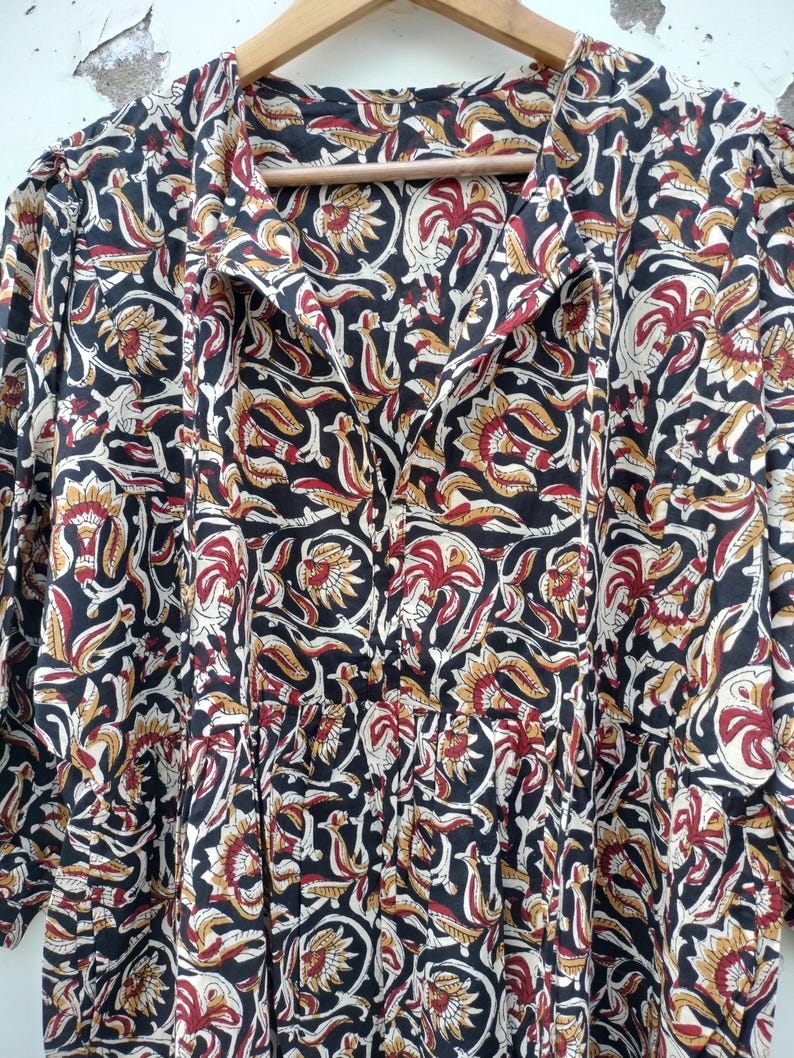 May include: A long-sleeved dress with a floral pattern in black, red, and gold. The dress has a collared neckline and buttons down the front. The fabric appears to be lightweight, suitable for warmer weather.