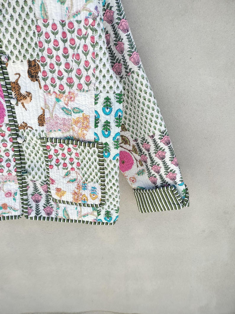 May include: A quilted jacket with a patchwork design featuring floral and animal motifs. The jacket has a white background with pink, green, and blue accents. The sleeves have a striped cuff. The jacket has a button closure and two pockets.