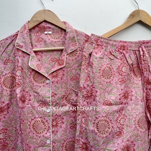 May include: A pink and green floral print pajama set with a white trim. The top has a button-up front and long sleeves. The pants have an elastic waistband.