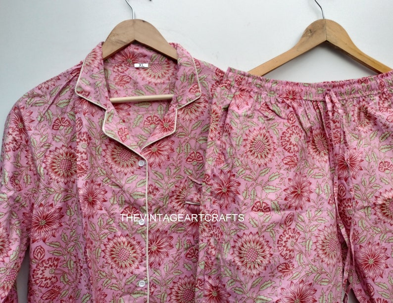 May include: A pink and green floral print pajama set with a white trim. The top has a button-up front and long sleeves. The pants have an elastic waistband.
