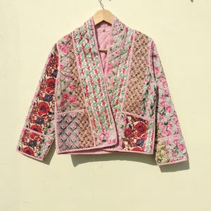 Pode incluir: Uma jaqueta acolchoada de patchwork com estampa floral em tons de rosa, vermelho e verde. A jaqueta tem um colar de xale e um fecho frontal.