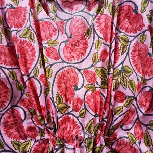 May include: A pink cotton kaftan with a floral print featuring red and green flowers. The kaftan has a V-neck and a drawstring waist.