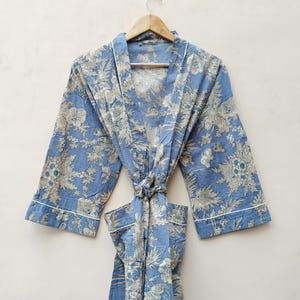 Op de afbeelding: Een blauwe badjas met een bloemenprint, witte afwerking en een strikceintuur.
