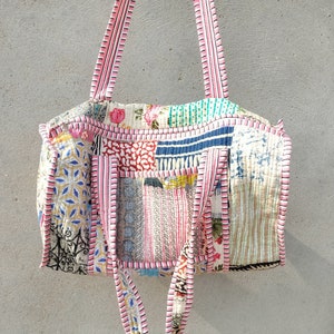 May include: A patchwork tote bag with pink and white striped straps. The bag is made of various fabrics with floral and geometric patterns in shades of blue, green, pink, and white.
