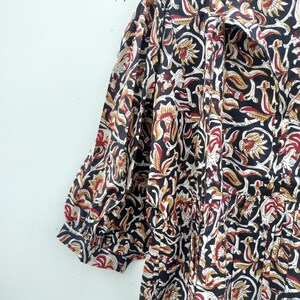 May include: A black, red, and cream-colored floral print dress with short sleeves. The fabric features a repeating pattern of stylized flowers and leaves. The dress has a collared neckline and gathered details.