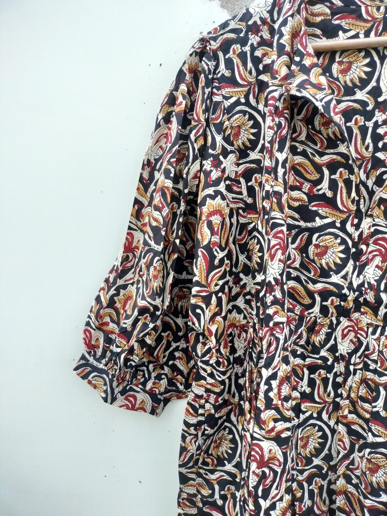 May include: A black, red, and cream-colored floral print dress with short sleeves. The fabric features a repeating pattern of stylized flowers and leaves. The dress has a collared neckline and gathered details.