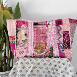 Puede incluir: Una bolsa de mano de lona de color rosa y blanco con parches, con motivos florales y geométricos. La bolsa tiene dos asas y está hecha de tela acolchada.