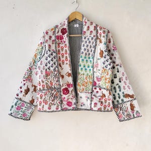 May include: A white quilted jacket with a patchwork design featuring colourful floral and animal prints. The jacket has a black and white striped lining and a black trim.