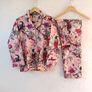May include: A peach-colored pajama set with a long-sleeved shirt and pants. The fabric features a floral print with colorful birds.