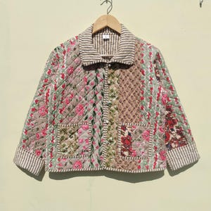 Puede incluir: Una chaqueta acolchada con un diseño de patchwork que presenta patrones florales en tonos de rosa, rojo, verde y marrón. La chaqueta tiene un cierre de botones en la parte delantera y dos bolsillos de parche.
