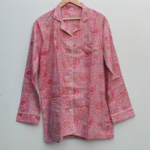 May include: A pink long-sleeved shirt with a floral print and white piping. The shirt has a button-up front and a collar.