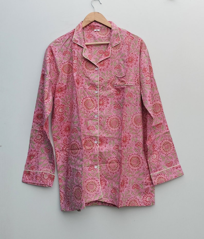 May include: A pink long-sleeved shirt with a floral print and white piping. The shirt has a button-up front and a collar.