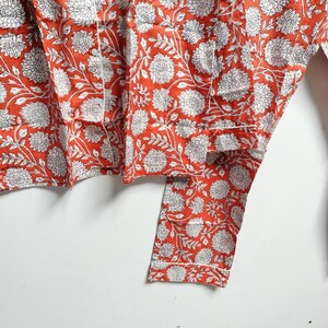 Puede incluir: Una tela de algod&oacute;n roja y blanca con estampado floral. La tela tiene un borde blanco y est&aacute; doblada por la mitad.