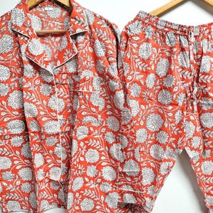 Puede incluir: Un conjunto de pijama rojo y blanco con estampado floral. La parte superior tiene un cuello abotonado y mangas largas. Los pantalones tienen una cintura el&aacute;stica y un cord&oacute;n.