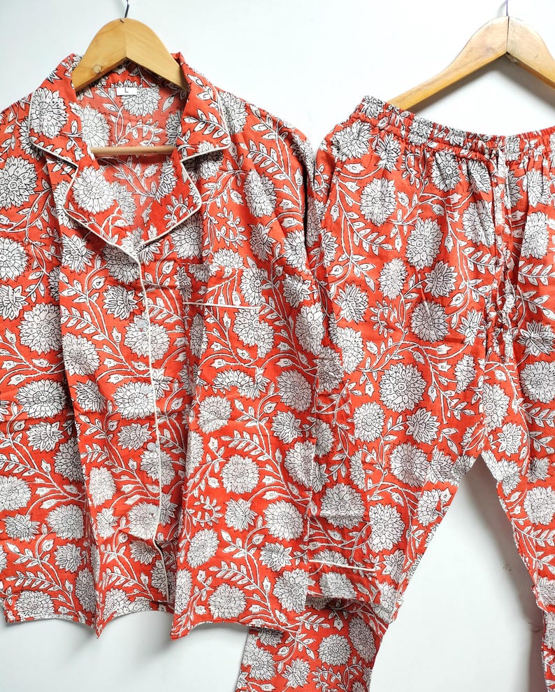 Puede incluir: Un conjunto de pijama rojo y blanco con estampado floral. La parte superior tiene un cuello abotonado y mangas largas. Los pantalones tienen una cintura el&aacute;stica y un cord&oacute;n.