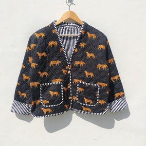 Pode incluir: Uma jaqueta acolchoada preta com fecho de botão e dois bolsos. A jaqueta é estampada com leopardos laranja e castanho.