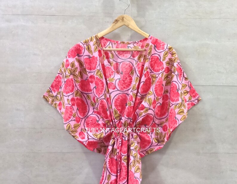 May include: A pink and red floral print kaftan with a V-neck and short sleeves. The kaftan has a tie at the waist and the text "THEVINTAGEARTCRAFTS" is printed on the bottom.
