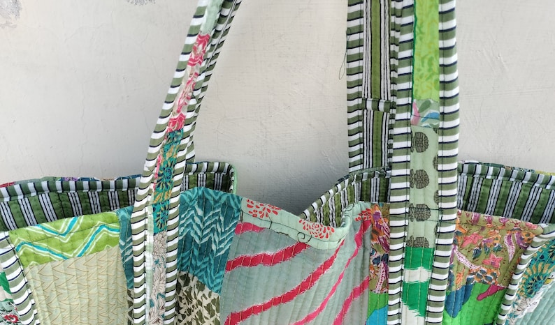 May include: A green patchwork tote bag with white and green striped handles. The bag is made of different fabrics with various patterns, including floral, geometric, and striped.