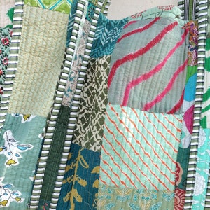 May include: A patchwork fabric bag with a variety of green, blue, and pink patterns. The bag is made of different pieces of fabric sewn together, creating a unique and colorful design.