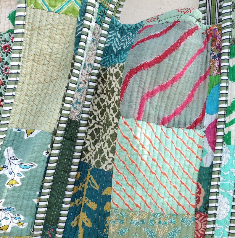 May include: A patchwork fabric bag with a variety of green, blue, and pink patterns. The bag is made of different pieces of fabric sewn together, creating a unique and colorful design.