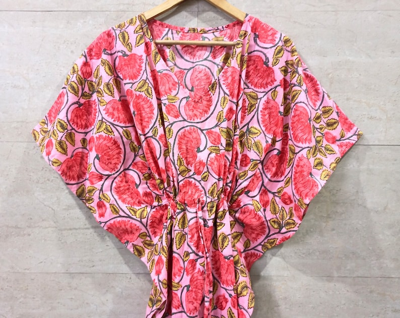 May include: A pink and gold floral print kaftan with a V-neck and short sleeves.