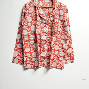 Puede incluir: Una camisa roja de manga larga con estampado floral blanco. La camisa tiene un cierre de botones en la parte delantera y un cuello.