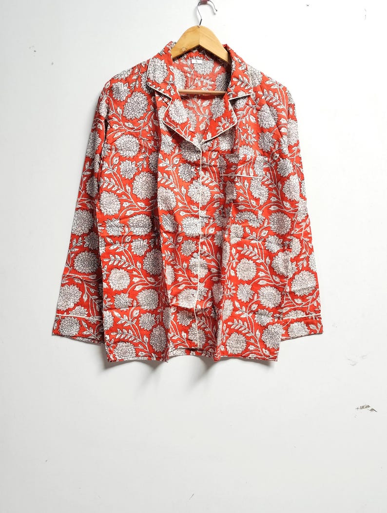 Puede incluir: Una camisa roja de manga larga con estampado floral blanco. La camisa tiene un cierre de botones en la parte delantera y un cuello.