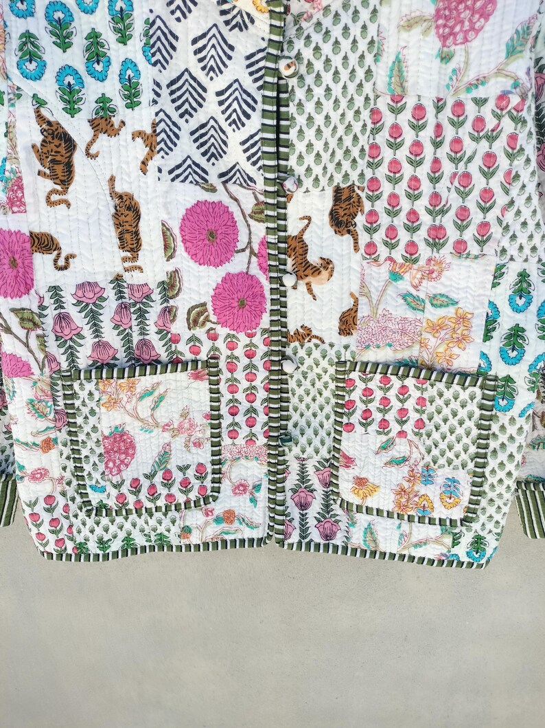 May include: A quilted jacket with a patchwork design. The jacket features various patterns, including tigers, flowers, and geometric shapes. The color palette includes white, pink, green, and brown. The jacket has two pockets and a button-up front.