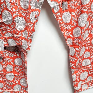 Puede incluir: Un pantal&oacute;n de algod&oacute;n naranja con estampado floral blanco. El pantal&oacute;n tiene un corte holgado y una cintura con cord&oacute;n.