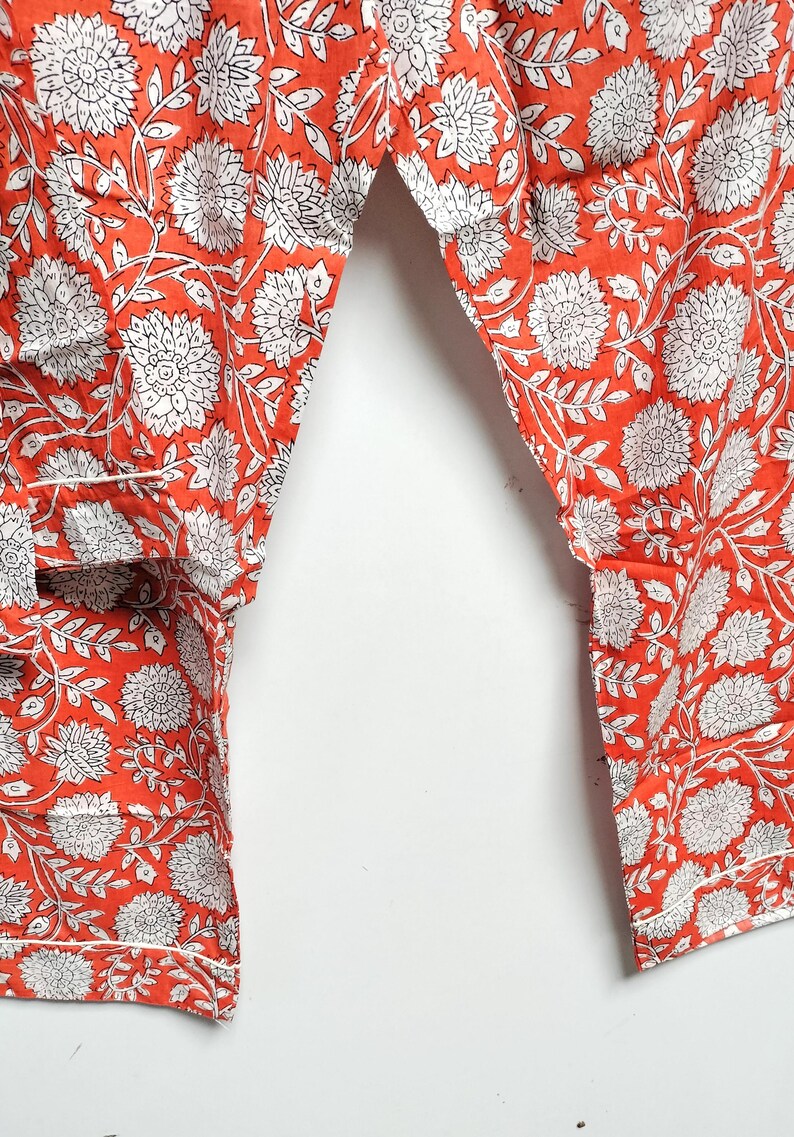 Puede incluir: Un pantal&oacute;n de algod&oacute;n naranja con estampado floral blanco. El pantal&oacute;n tiene un corte holgado y una cintura con cord&oacute;n.