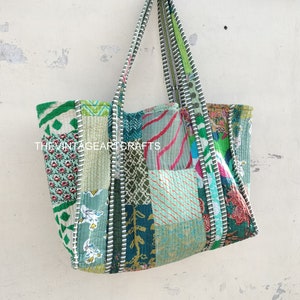 May include: A patchwork tote bag with a green, blue, and pink color scheme. The bag has a long strap and is made of quilted fabric.
