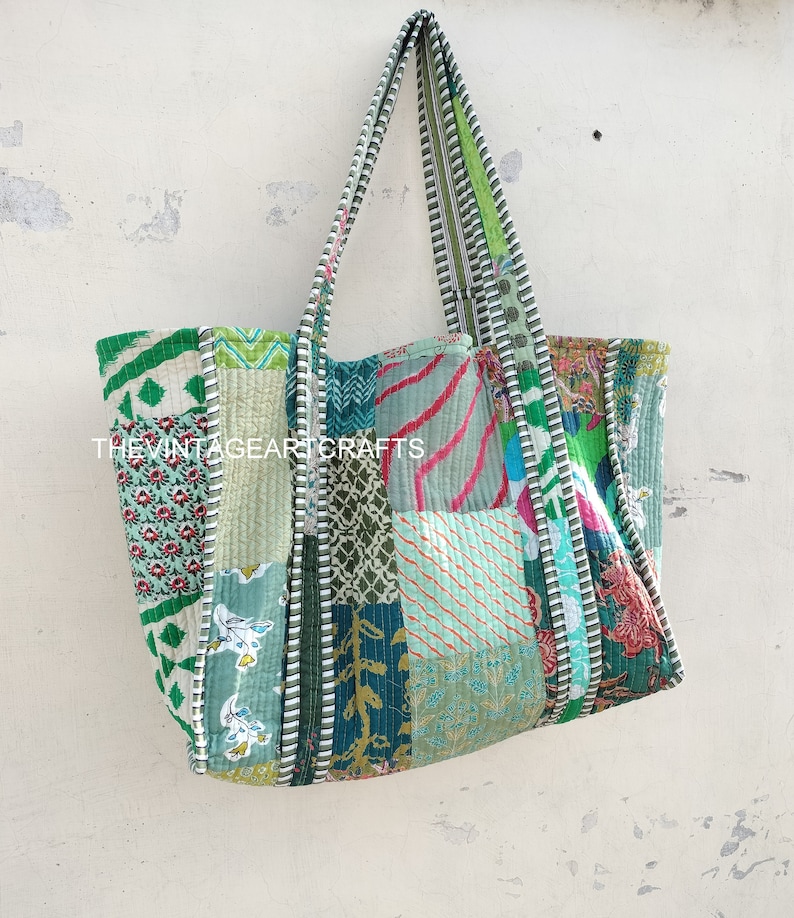 May include: A patchwork tote bag with a green, blue, and pink color scheme. The bag has a long strap and is made of quilted fabric.