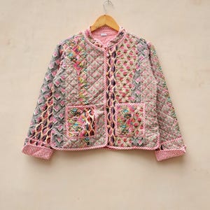 Pode incluir: Uma jaqueta acolchoada com estampa floral e acabamento em listras rosa e branco. A jaqueta tem fecho de botão e dois bolsos.