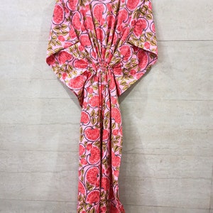 May include: A pink kaftan with a floral print featuring red flowers and green leaves. The kaftan has a gathered waist and short sleeves.