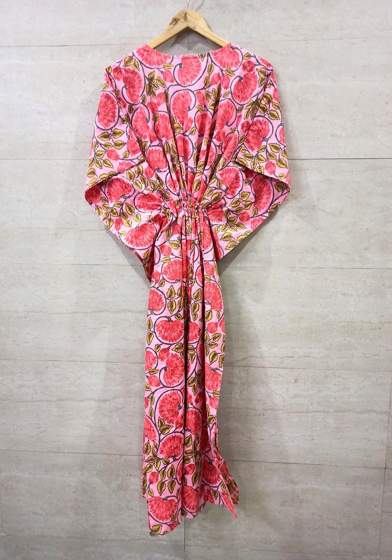 May include: A pink kaftan with a floral print featuring red flowers and green leaves. The kaftan has a gathered waist and short sleeves.